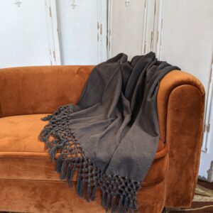 Grey blanket with knit tassels displayed over auburn colored couch