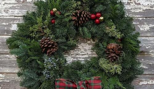 Fresh evergreen wreath decorated with red plaid bow, pinecones, and shiny berries